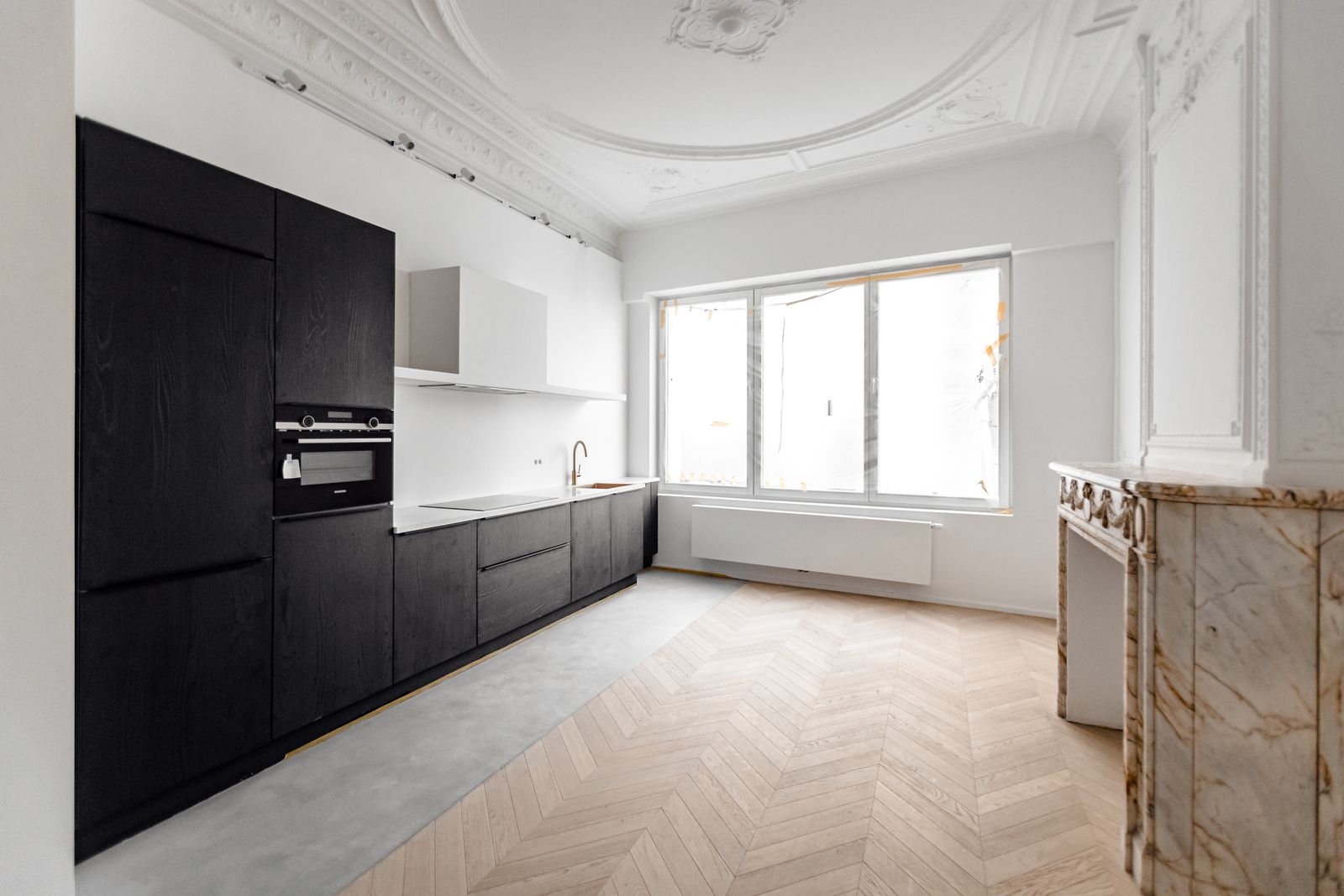 Zwarte keuken over de volle wand in een kamer met ornamentplafond, visgraatparket en een marmeren schouw